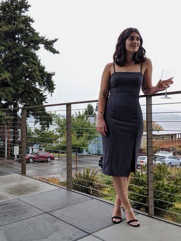 Sara standing by a railing wearing gray, knee-length spaghetti strap dress