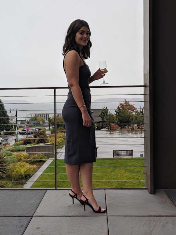 Profile of Sara in gray sheath dress and black sandals with gold chain ankle strap